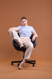 Photo of Beautiful young woman sitting on armchair against brown background