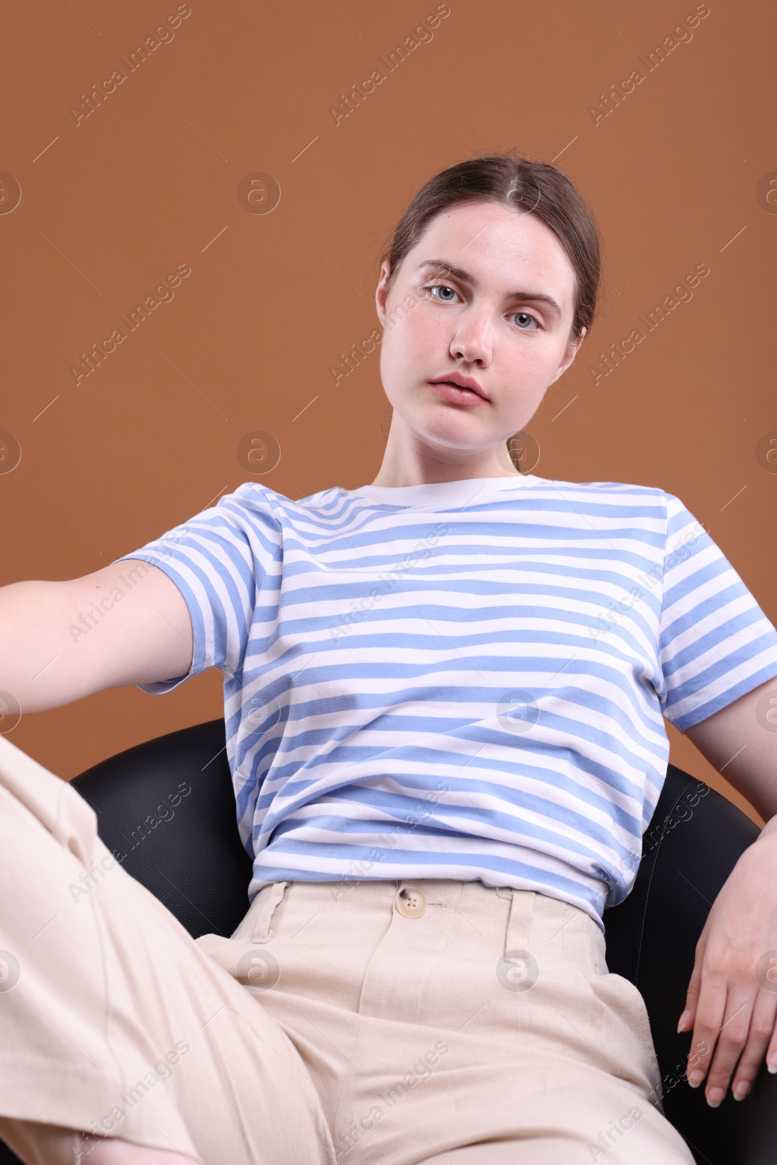 Beautiful young woman sitting on armchair against brown background Photo of Beautiful young woman sitting on armchair against brown background