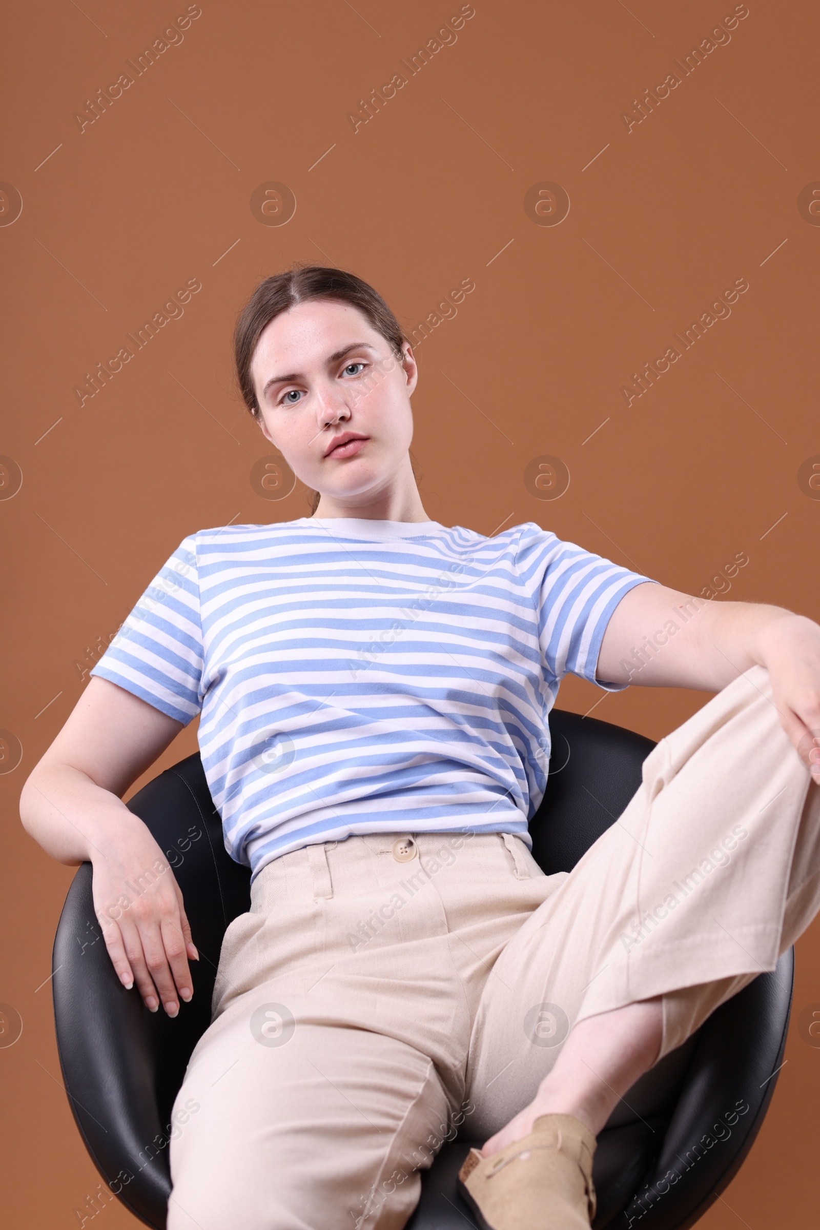 Beautiful young woman sitting on armchair against brown background Photo of Beautiful young woman sitting on armchair against brown background
