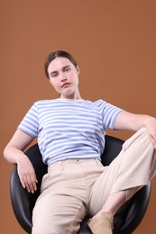Photo of Beautiful young woman sitting on armchair against brown background