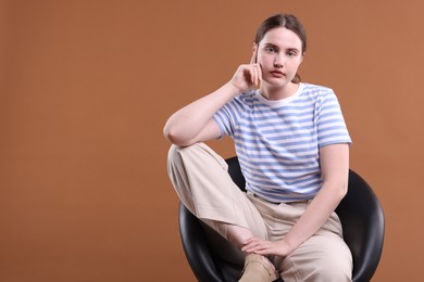 Photo of Beautiful young woman sitting on armchair against brown background, space for text