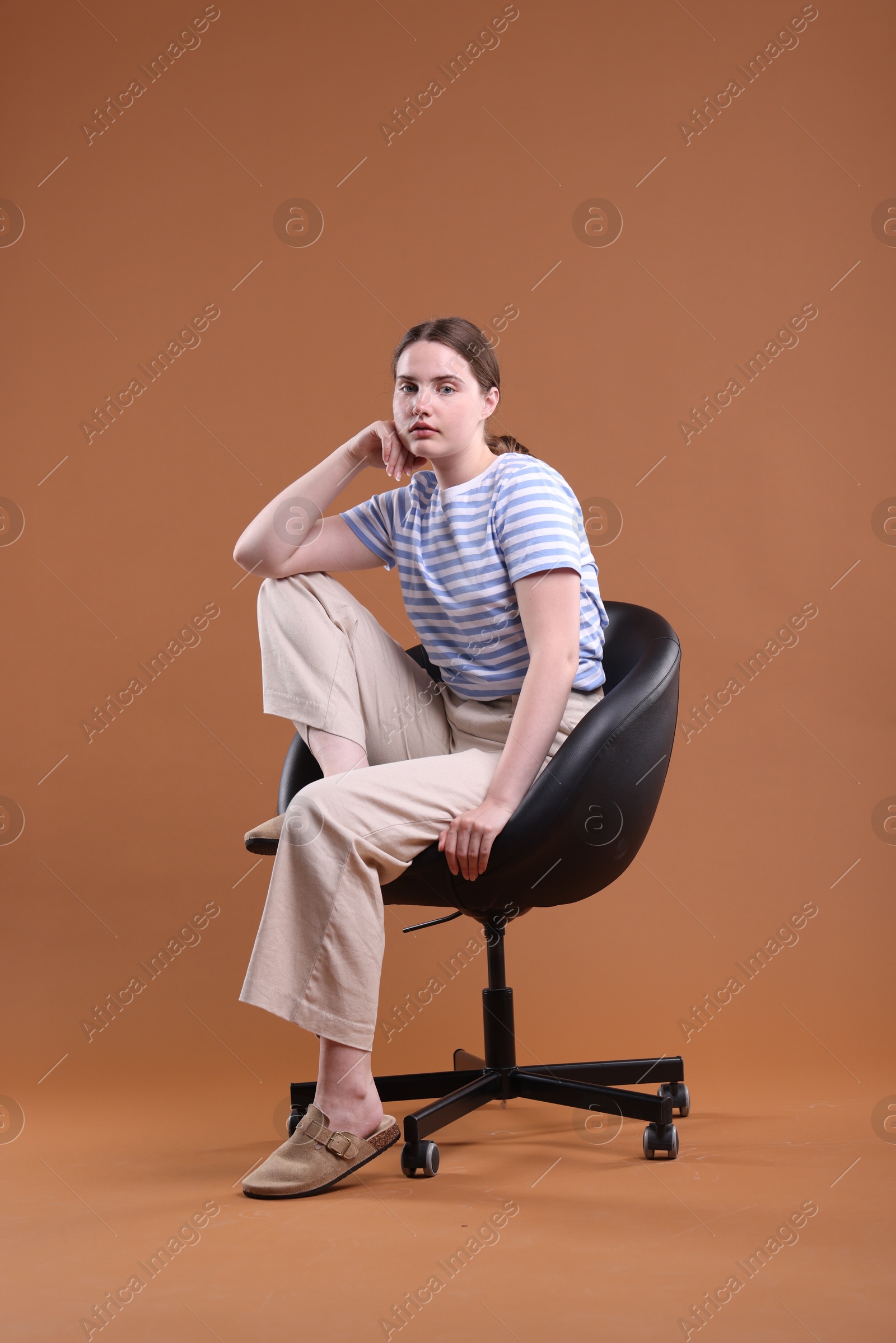 Beautiful young woman sitting on armchair against brown background Photo of Beautiful young woman sitting on armchair against brown background