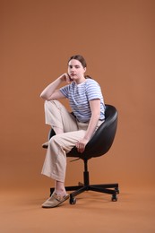 Photo of Beautiful young woman sitting on armchair against brown background
