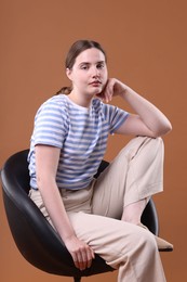Photo of Beautiful young woman sitting on armchair against brown background