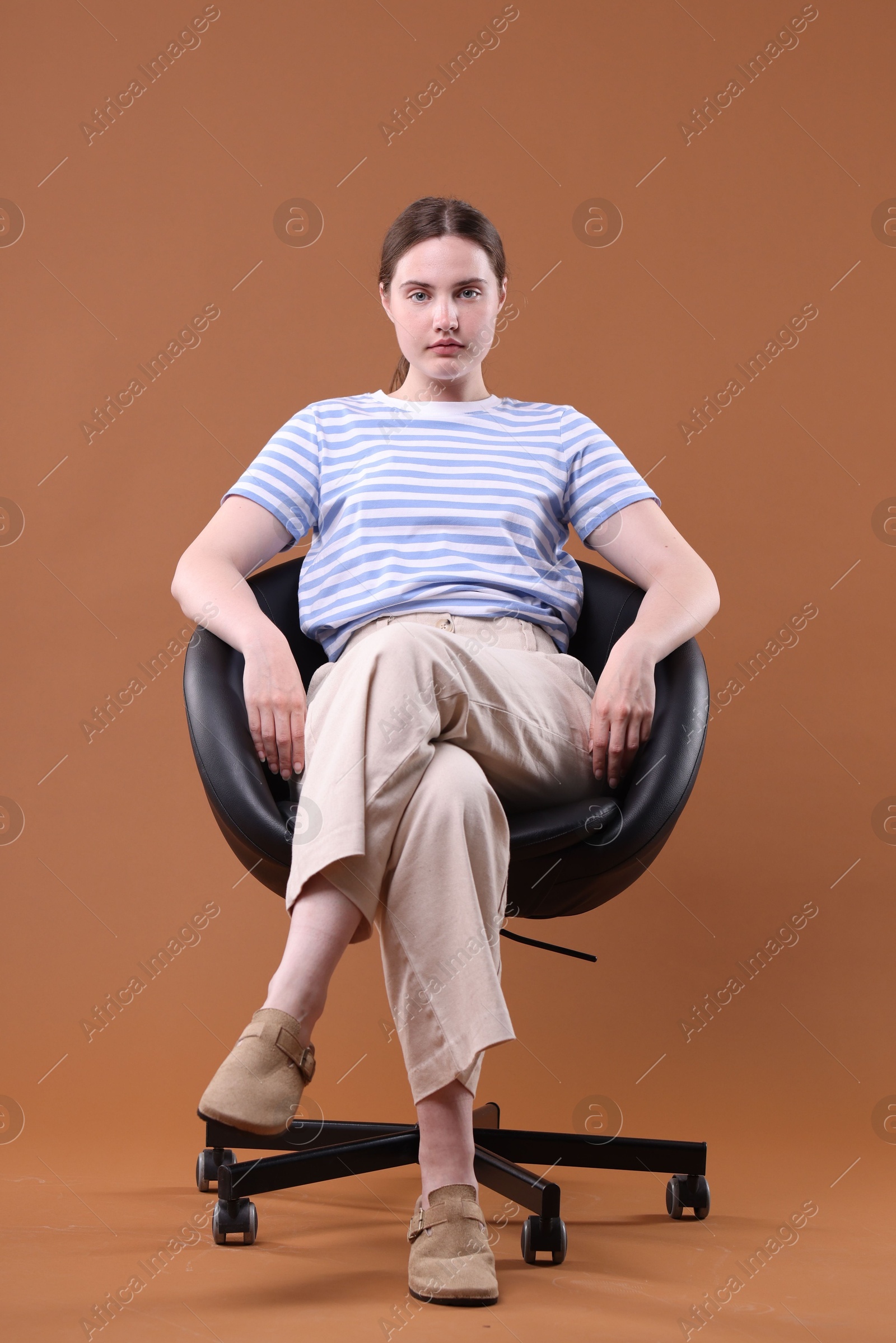 Beautiful young woman sitting on armchair against brown background Photo of Beautiful young woman sitting on armchair against brown background