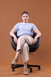 Photo of Beautiful young woman sitting on armchair against brown background