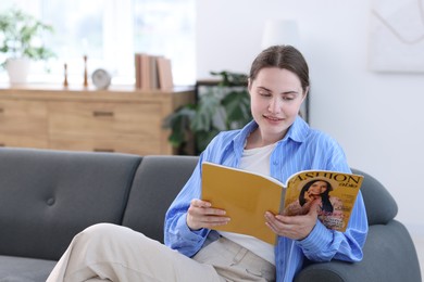 Photo of Woman reading lifestyle magazine on sofa at home