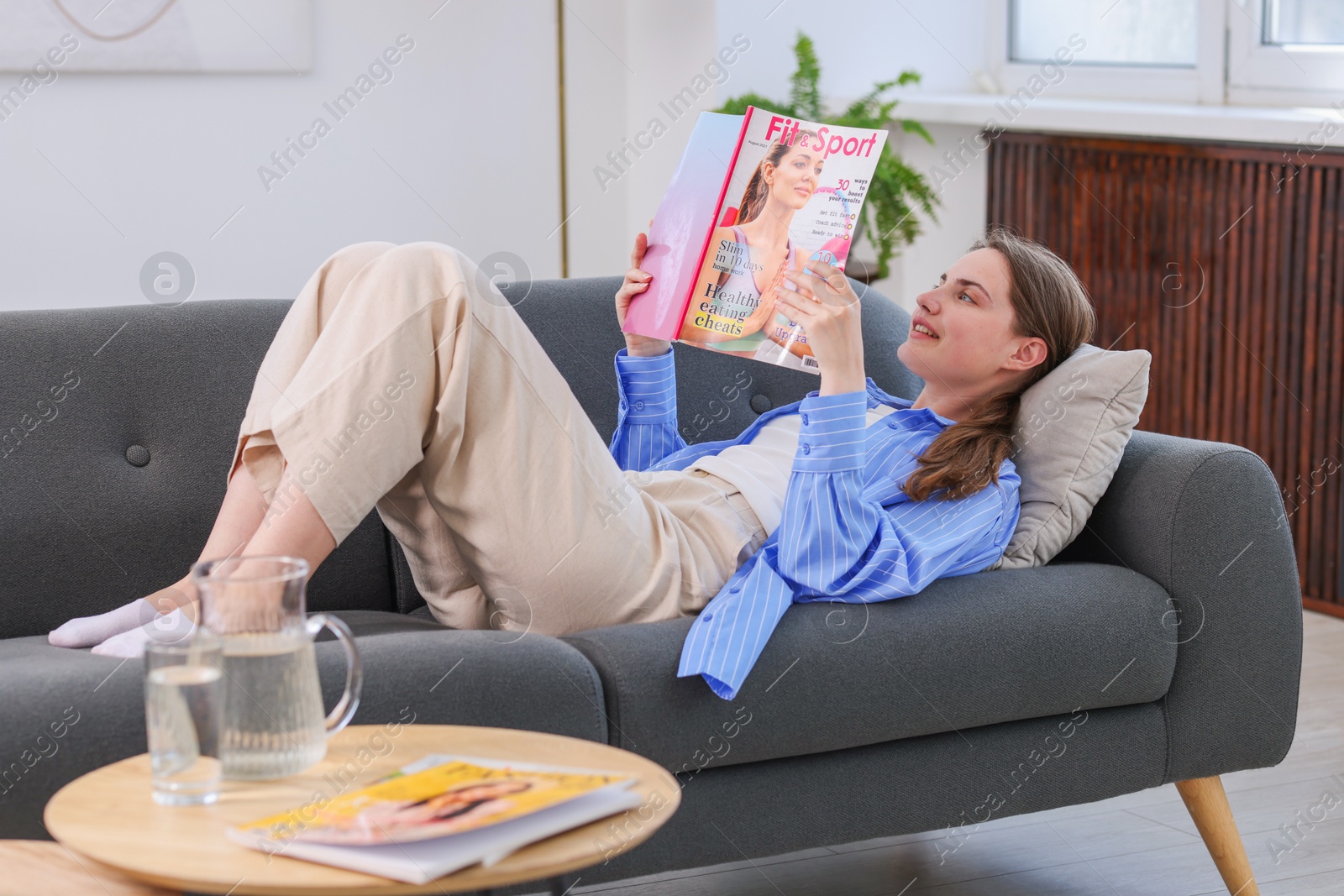 Photo of Woman reading lifestyle magazine on sofa at home