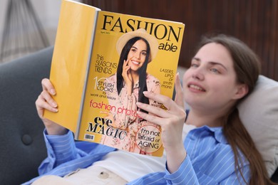Photo of Woman reading fashion magazine on sofa at home, selective focus
