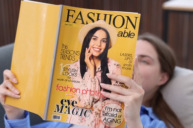 Photo of Woman reading fashion magazine on sofa at home, selective focus