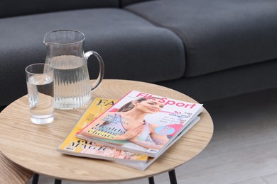Photo of Lifestyle magazines and water on coffee table indoors, closeup
