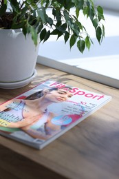 Photo of Lifestyle magazine and houseplant on wooden table indoors, closeup