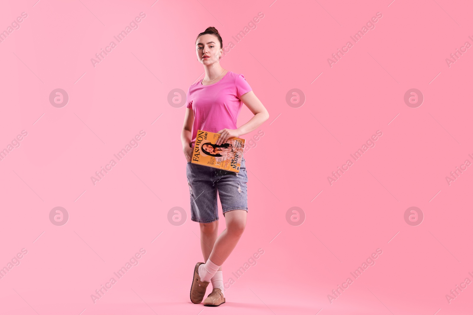 Woman with fashion magazine on pink background Photo of Woman with fashion magazine on pink background