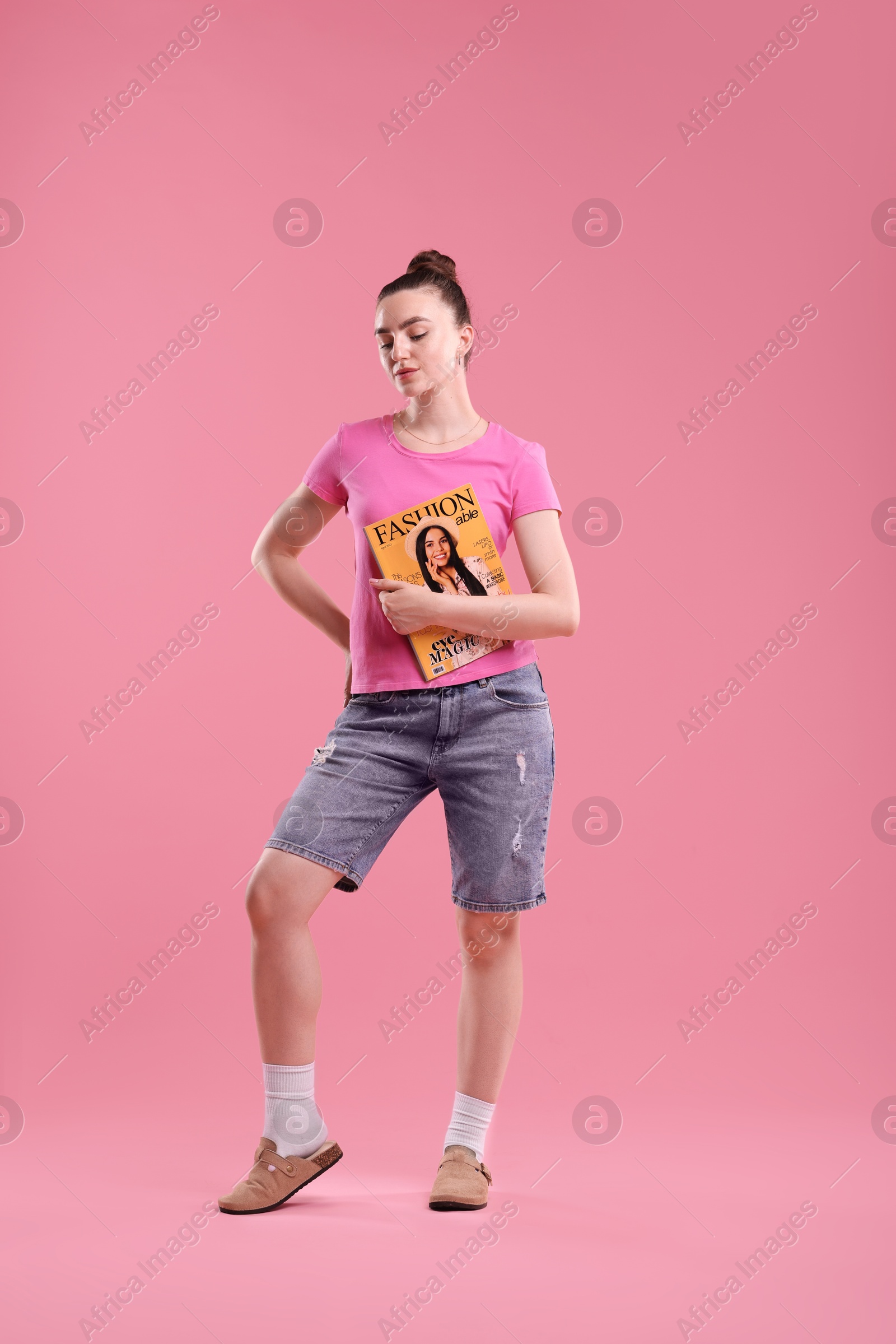 Woman with fashion magazine on pink background Photo of Woman with fashion magazine on pink background
