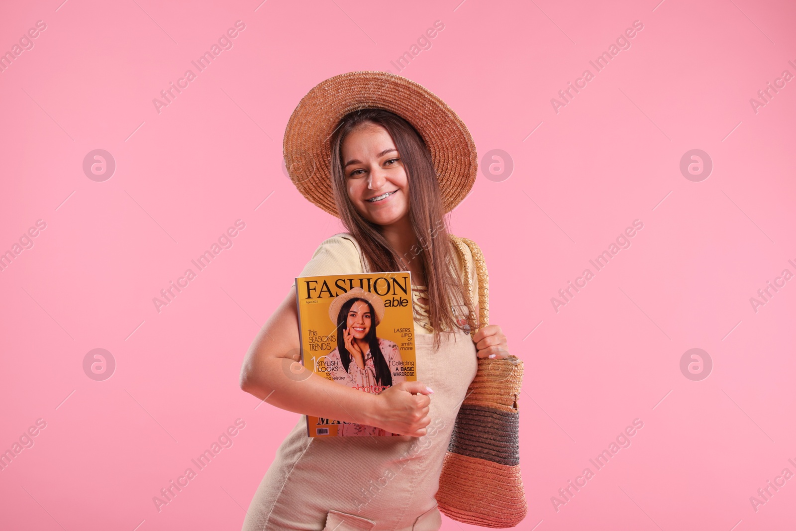 Woman with fashion magazine and bag on pink background Photo of Woman with fashion magazine and bag on pink background