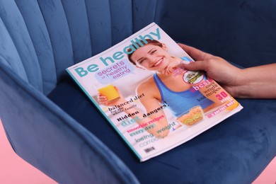 Photo of Woman with lifestyle magazine and armchair on pink background, closeup