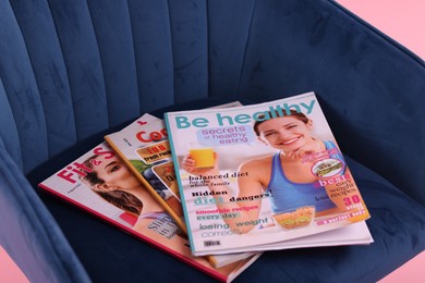 Photo of Different lifestyle magazines on armchair on pink background, closeup