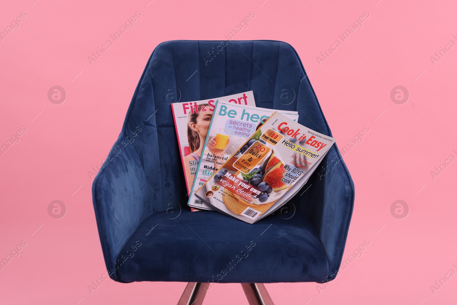 Photo of Different lifestyle magazines on armchair on pink background, closeup