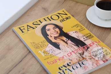 Photo of Fashion magazine and cup of coffee on wooden table indoors, closeup