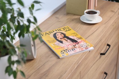 Photo of Fashion magazine and cup of coffee on wooden table indoors