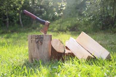 Photo of Metal axe, chopped firewood and wooden log on green grass outdoors