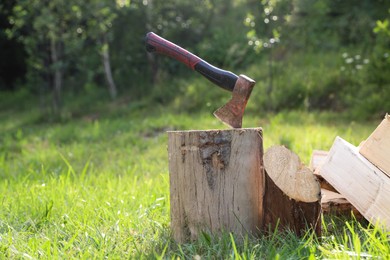 Photo of Metal axe, chopped firewood and wooden log on green grass outdoors. Space for text