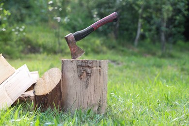 Photo of Metal axe, chopped firewood and wooden log on green grass outdoors. Space for text