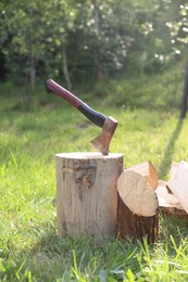 Photo of Metal axe, chopped firewood and wooden log on green grass outdoors