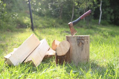 Photo of Metal axe, chopped firewood and wooden log on green grass outdoors