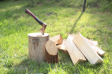 Photo of Metal axe, chopped firewood and wooden log on green grass outdoors