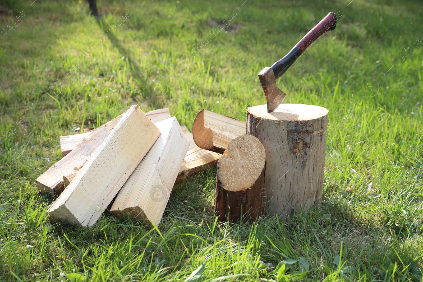 Metal axe, chopped firewood and wooden log on green grass outdoors Photo of Metal axe, chopped firewood and wooden log on green grass outdoors