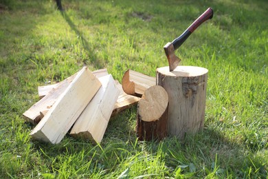 Photo of Metal axe, chopped firewood and wooden log on green grass outdoors