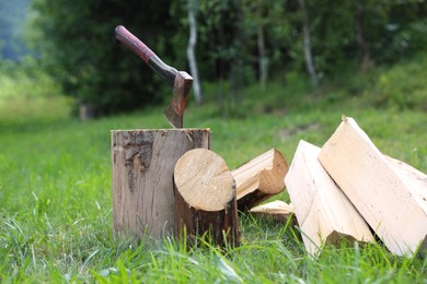 Photo of Metal axe, chopped firewood and wooden log on green grass outdoors
