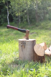 Photo of Metal axe, chopped firewood and wooden log on green grass outdoors