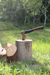 Photo of Metal axe, chopped firewood and wooden log on green grass outdoors