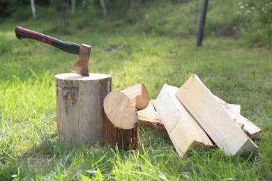 Photo of Metal axe, chopped firewood and wooden log on green grass outdoors