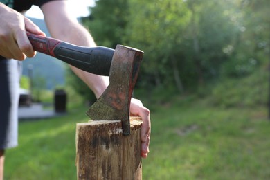 Photo of Man chopping firewood with axe outdoors, closeup