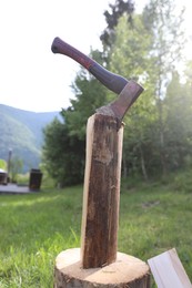 Photo of Metal axe with firewood and wooden log outdoors