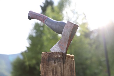 Photo of Metal axe on wooden log outdoors, closeup