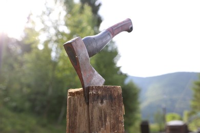 Photo of Metal axe on wooden log outdoors, closeup