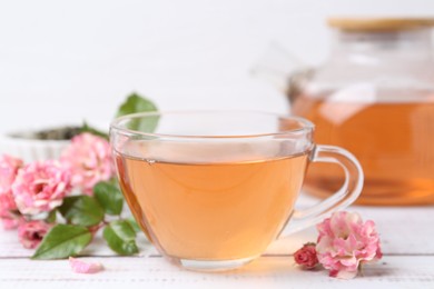 Photo of Tasty rose tea in glass cup and flowers on white wooden table, closeup
