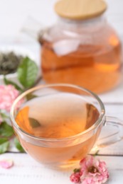 Photo of Tasty rose tea in glass cup and flowers on white wooden table, closeup