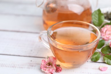 Photo of Tasty rose tea and flowers on white wooden table, closeup. Space for text