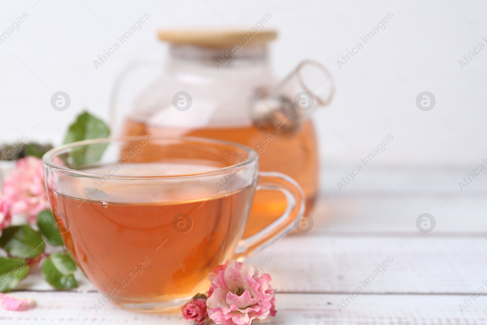 Tasty rose tea and flowers on white wooden table, closeup. Space for text Photo of Tasty rose tea and flowers on white wooden table, closeup. Space for text