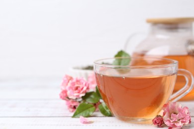 Photo of Tasty rose tea and flowers on white wooden table, closeup. Space for text