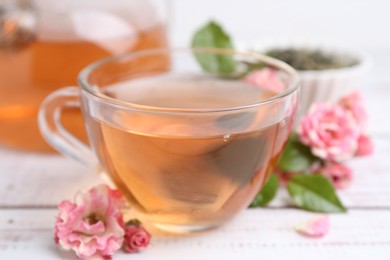 Photo of Tasty rose tea in glass cup and flowers on white wooden table, closeup