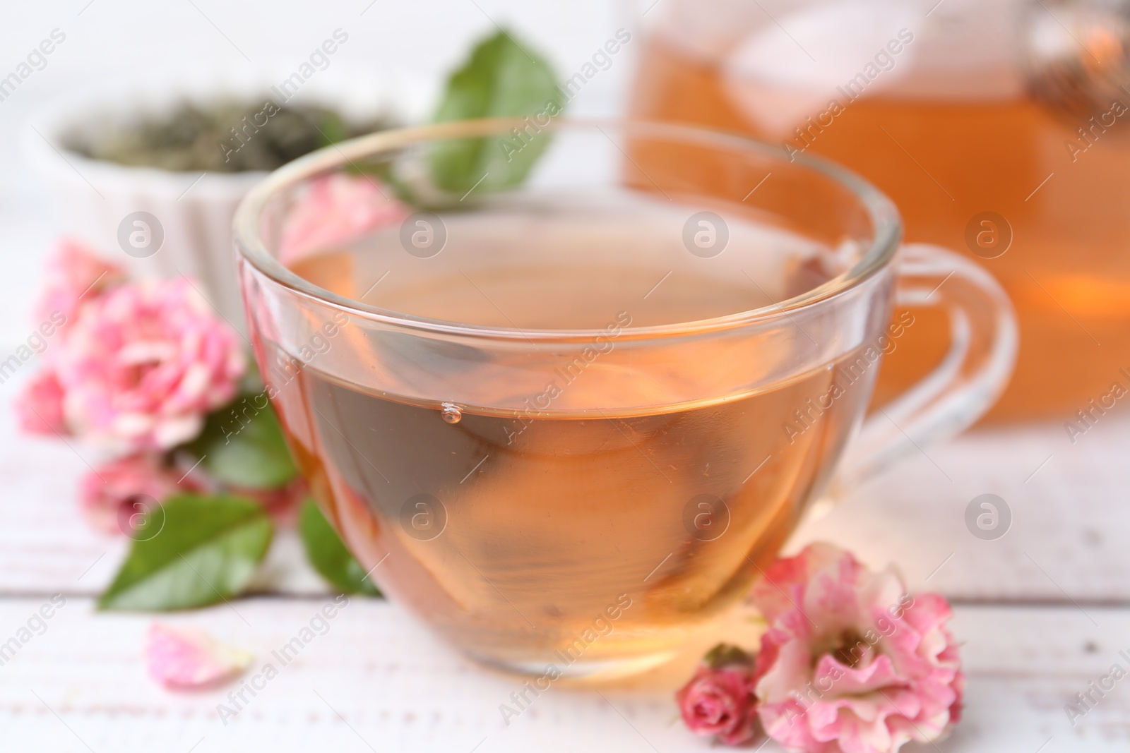 Tasty rose tea in glass cup and flowers on white wooden table, closeup Photo of Tasty rose tea in glass cup and flowers on white wooden table, closeup