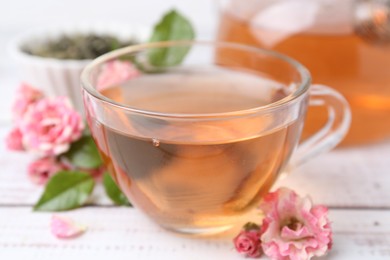 Photo of Tasty rose tea in glass cup and flowers on white wooden table, closeup