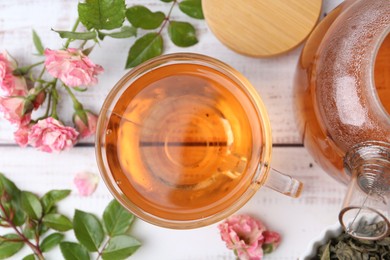 Photo of Tasty rose tea in glass cup, flowers and leaves on light wooden table, flat lay