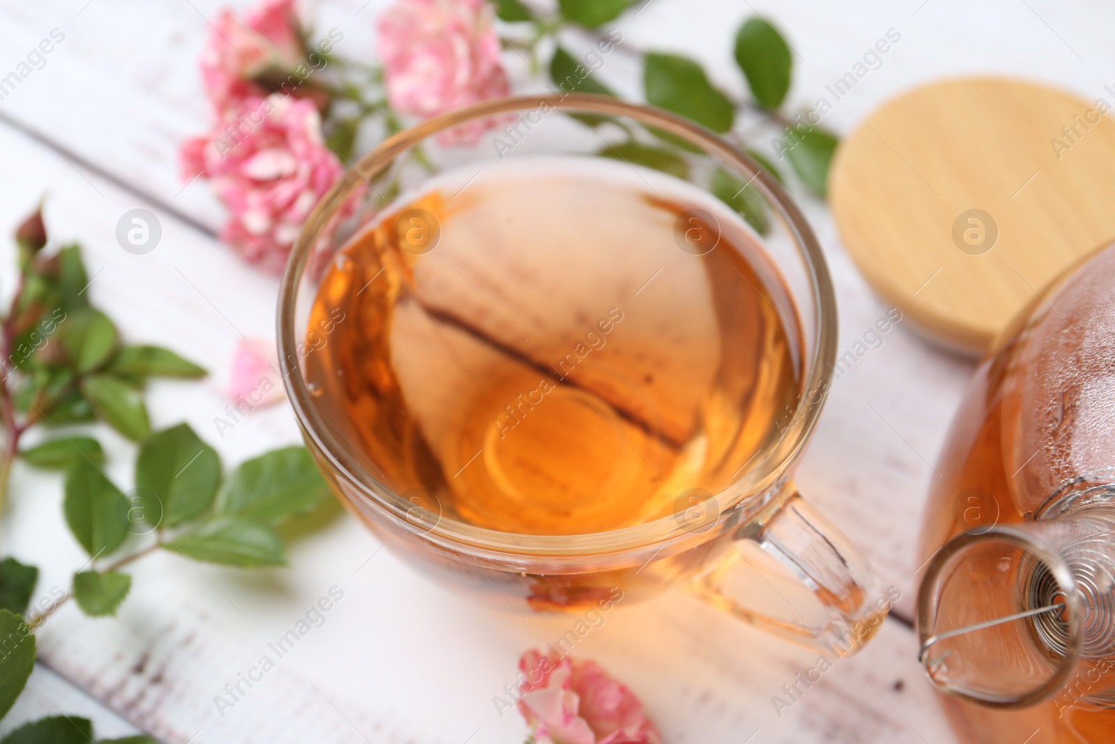 Tasty rose tea in glass cup, flowers and leaves on white wooden table, closeup Photo of Tasty rose tea in glass cup, flowers and leaves on white wooden table, closeup